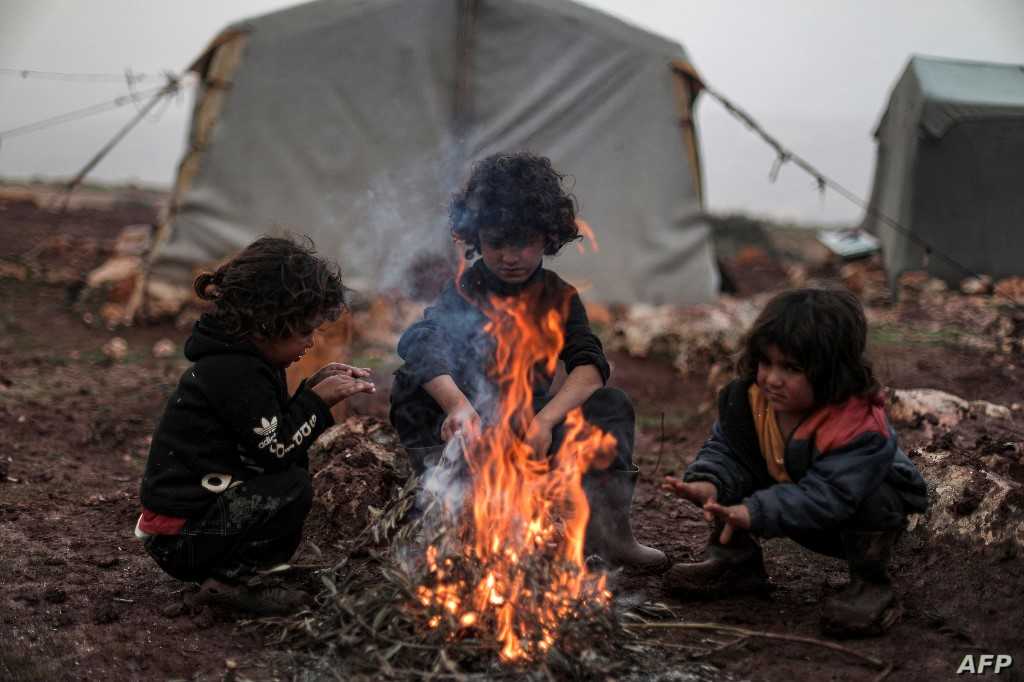 Children from the Syrian family of Abou Hussein, who fled the countryside of Hama province four years prior, warm up around a bonfire of burning olive branches at a make-shift camp for the displaced by the village of Babisqa in Syria's northwestern rebel-held province of Idlib on December 17, 2021. - Winter usually spells tragedy for northwest Syria, home to more than three million people, nearly half of whom have been displaced by a decade-long war that has killed nearly half a million. In makeshift camps in the country's last major rebel enclave, streets turn muddy, tents leak and inhabitants die of hypothermia or in fires caused by unsafe heating methods. (Photo by Aaref WATAD / AFP)